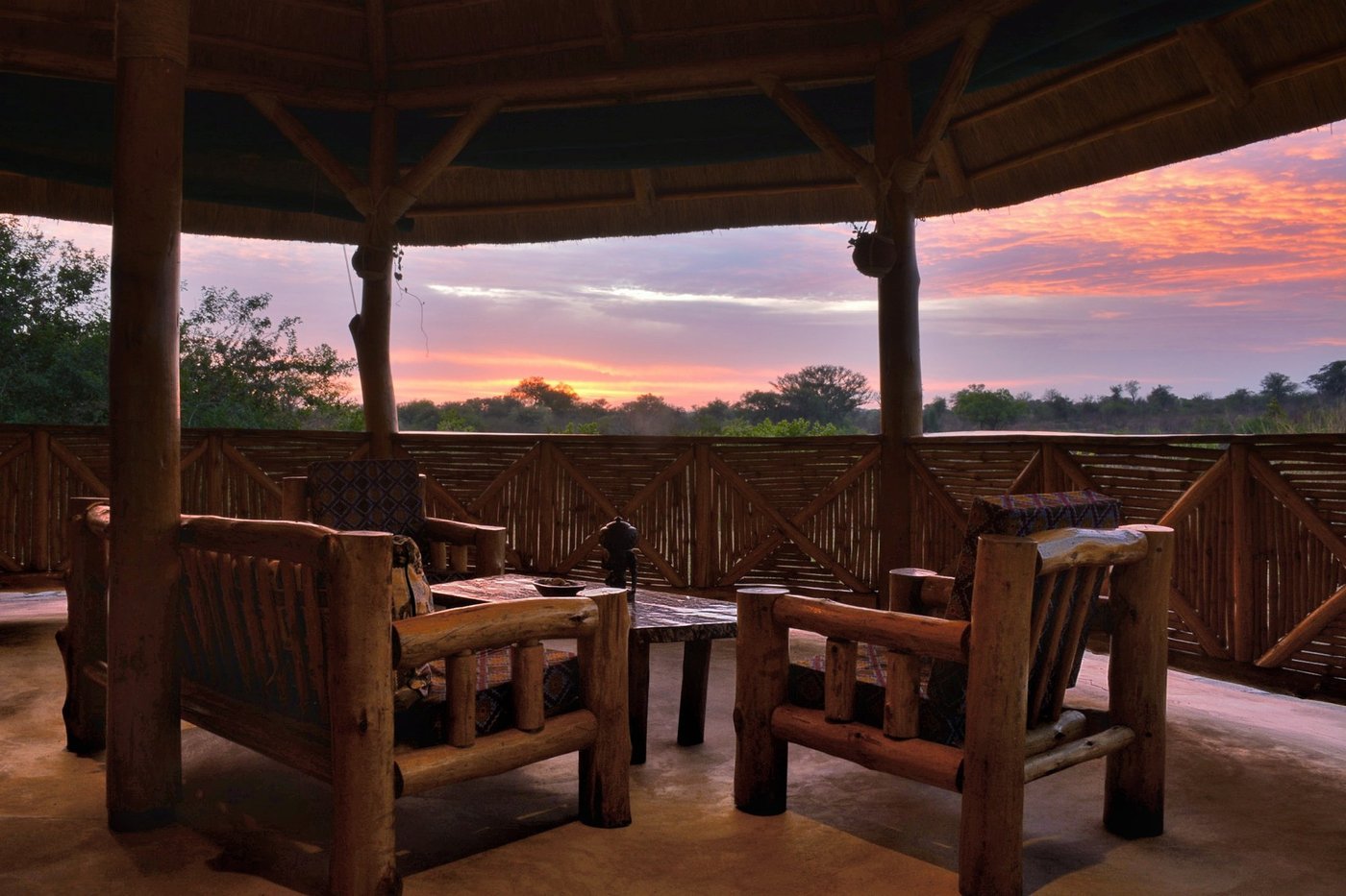 Offene Bambuslounge mit Holzstühlen, die auf den Abendhimmel blicken, in der Bamboo Village Safari Lodge