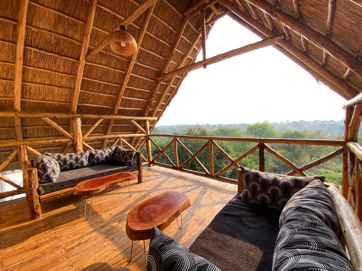 Erhöhte Bambusterrasse mit gepolsterten Sitzplätzen mit Blick auf das Buschland in der Bamboo Village Safari Lodge