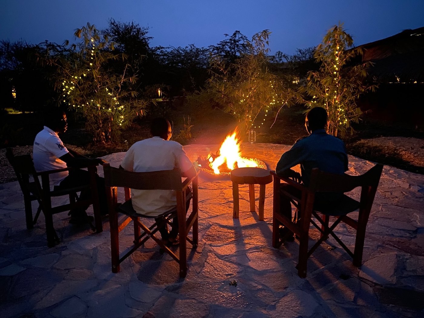 Gäste um die Feuerstelle bei Einbruch der Dunkelheit in der Bamboo Village Safari Lodge