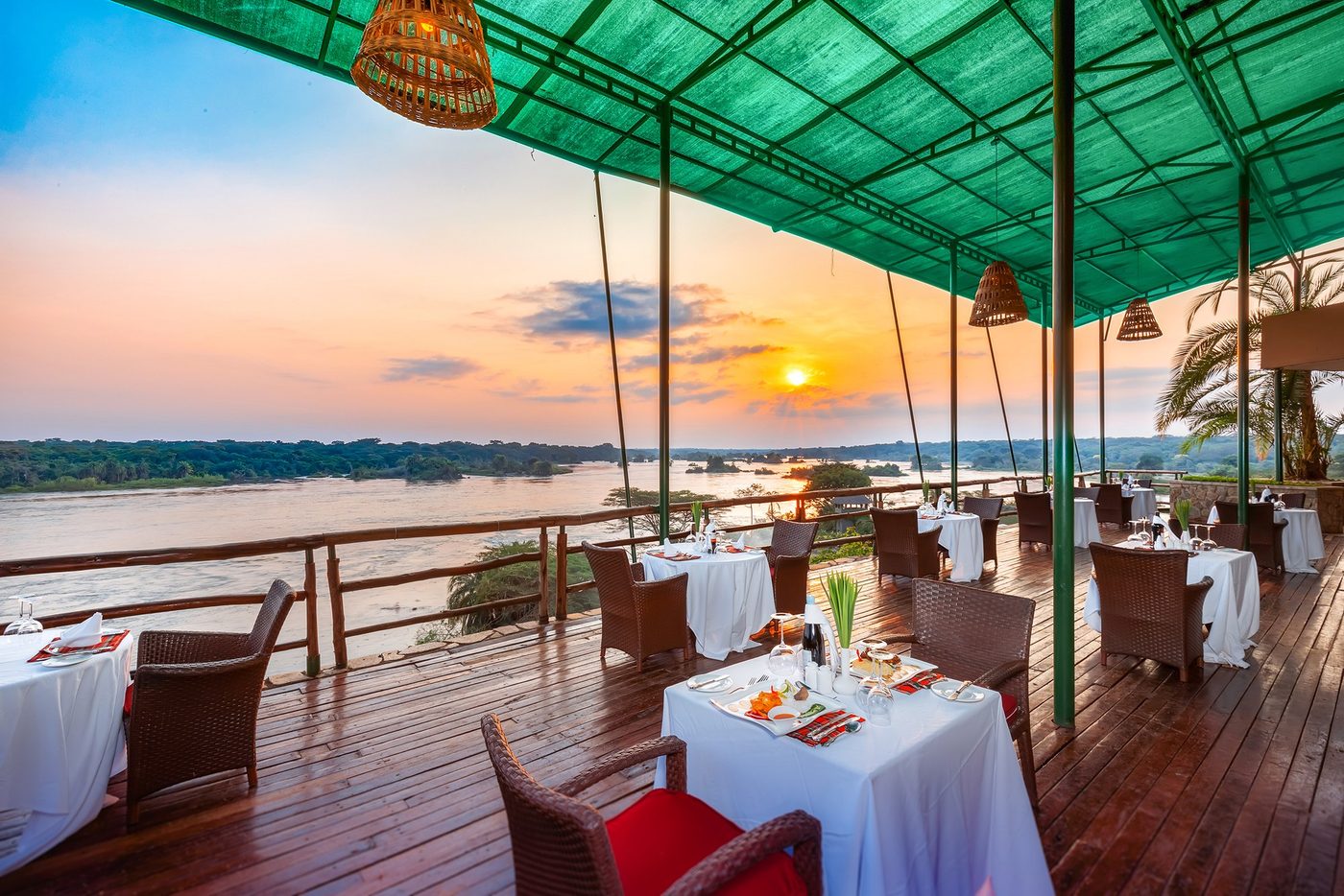 Terrasse de restaurant au bord de la rivière sous un toit en auvent vert au coucher du soleil à Chobe Safari Lodge