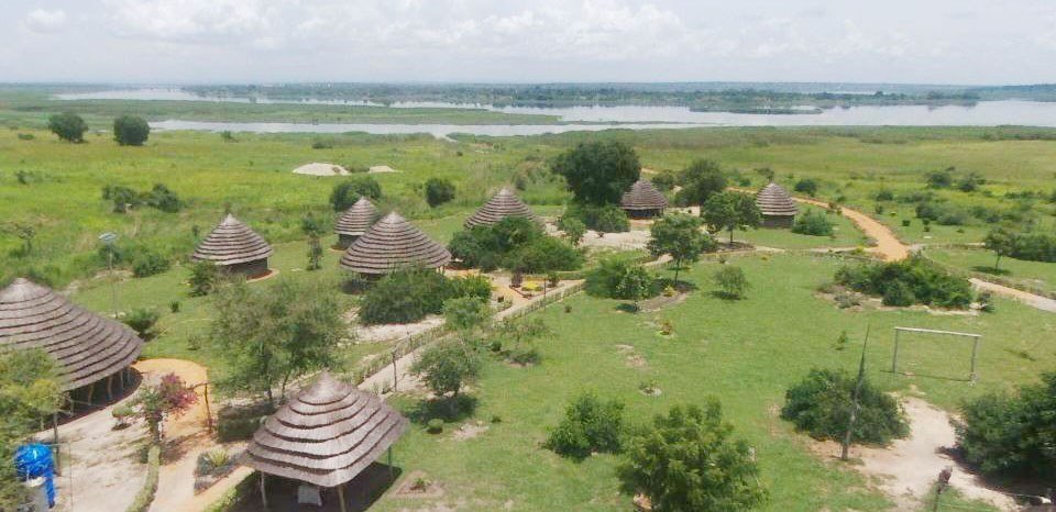 Rieten rondavels en grasvelden strekken zich uit boven de Nile op Heritage Safari Lodge in Murchison Falls