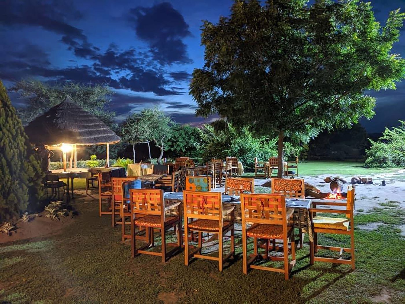 Strohgedecktes Banda bei Dämmerung mit Outdoor-Esstisch im Heritage Safari Lodge, Murchison Falls