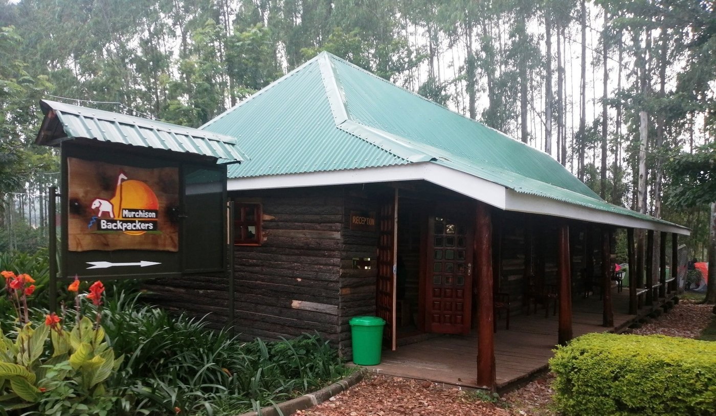 Houten ingangsgebouw van Murchison Backpackers met bord en bloeiende struiken, Murchison Falls