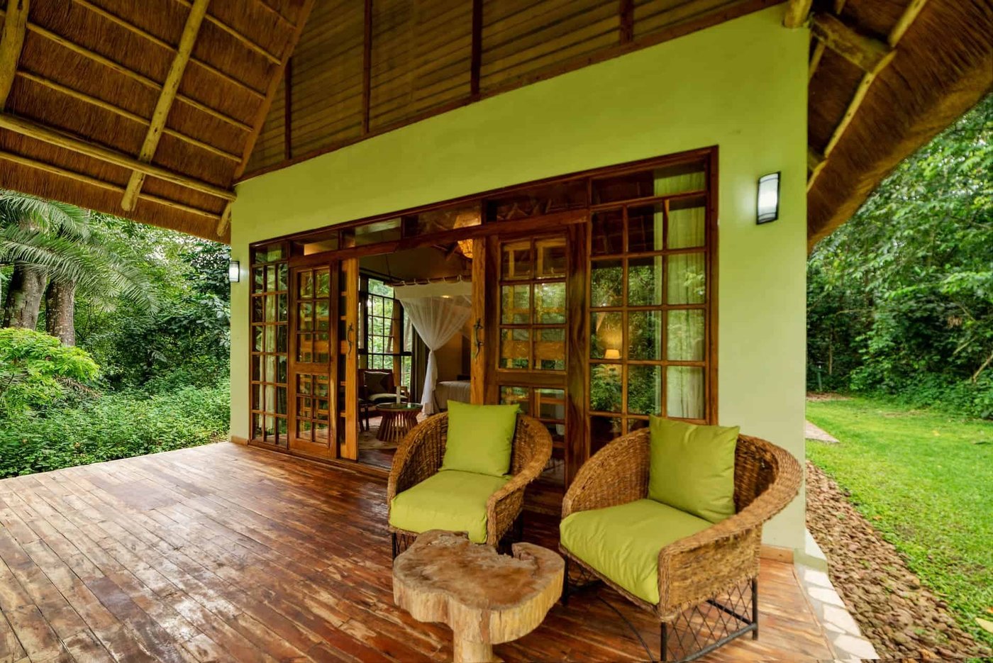 Terrasse circulaire avec des chaises rembourrées vertes parmi les arbres forestiers à Pabidi Lodge