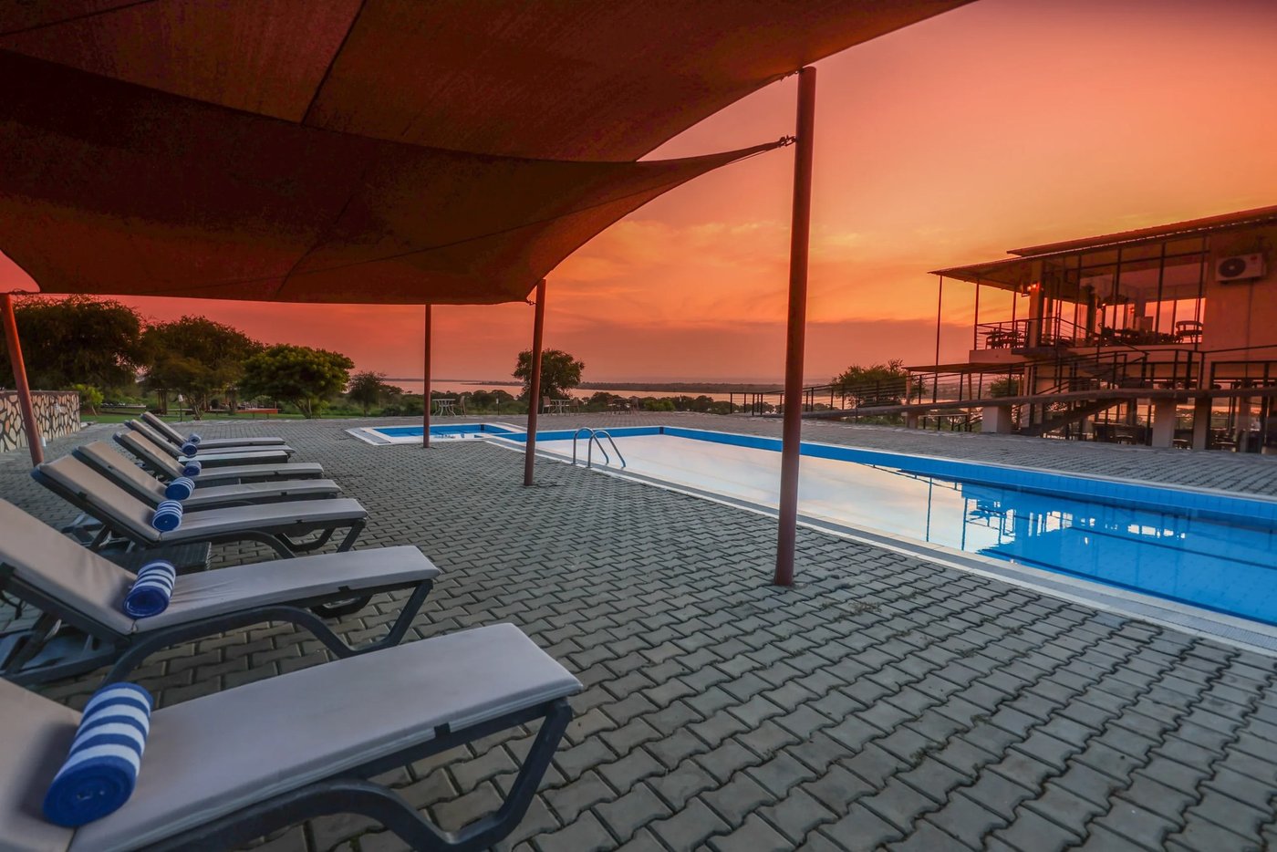 Pooldeck und Liegestühle unter einem Sonnensegel bei Dämmerung in Pakuba Safari Lodge