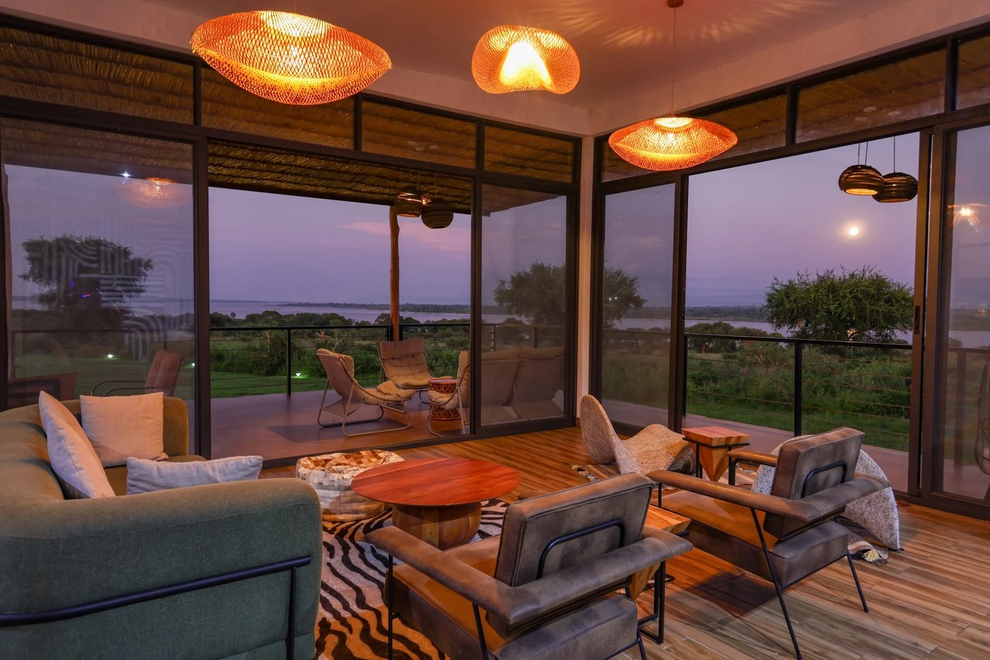 Loungeplätze an Boden-zu-Decke-Fenstern bei Sonnenuntergang in Pakuba Safari Lodge