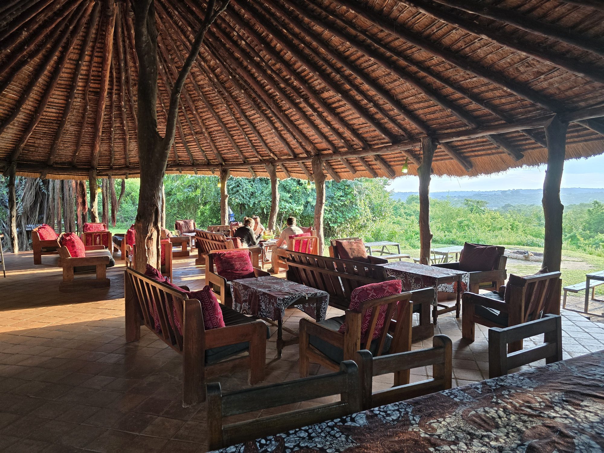 The main bar mid-morning, guests at the tables under the big thatch and the bush stretching away below